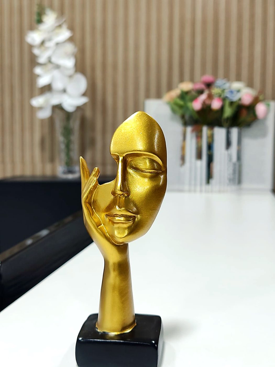 Escultura dourada de um rosto feminino com a mão no rosto, na recepção do Studio